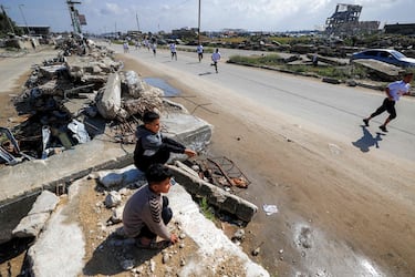 Unos niños sentados entre los escombros observan a los corredores participantes en una maratón organizada por la fundación Al-Faris al-Shahm, con sede en los Emiratos Árabes Unidos, en el campamento de refugiados palestinos de Bureij, en el centro de la Franja de Gaza. La violencia ha persistido en Gaza a pesar del alto el fuego de octubre de 2025.