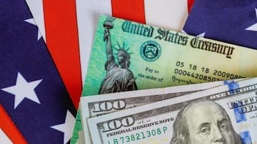 Cheque del Departamento del Tesoro de Estados Unidos sobre la bandera estadounidense y billetes de cien d&oacute;lares.