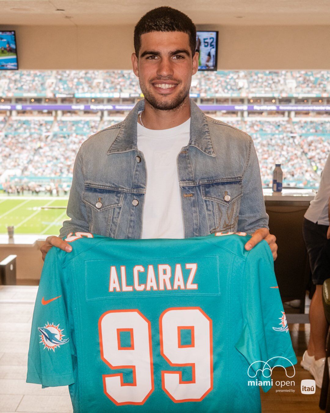 El tenista español Carlos Alcaraz posa con una camiseta de los Miami Dolphins en el Hard Rock Stadium de Miami