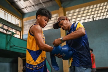 Un entrenador ayuda a un joven a ponerse los guantes de boxeo antes del inicio de la práctica. 