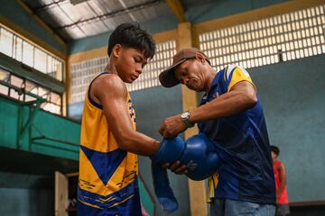 Un entrenador ayuda a un joven a ponerse los guantes de boxeo antes del inicio de la pr¨¢ctica.