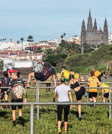 Atletas de la Bestial Race Gran Canaria superando un obstáculo con paisaje urbano de fondo.
