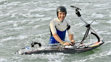 Rub&eacute;n Alc&aacute;ntara, con casco y neopreno, agarrando el invento que mezcla surf y bici en el mar. 