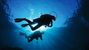 Two scuba divers silhouetted against the sun while they explore a coral reef