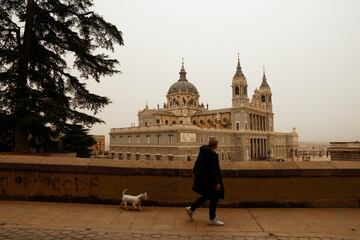 Un hombre camina junto a su perro cerca de la Catedral de la Almudena rodeado del polvo sahariano traído por la tormenta Celia.