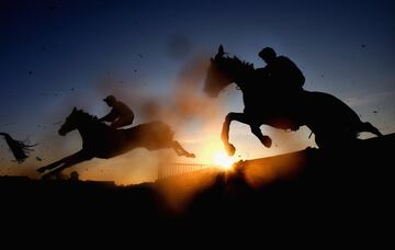 Dos jinetes saltan una cerca durante la carrera de obstáculos de los Cliftons of Wrexham Novices en el hipódromo de Bangor, Gales.