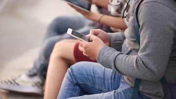Unrecognizable group of friends in casualwear gathered together outdoors and using their devices, close-up shot