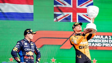 Lando Norris alza el trofeo de ganador en Holand con Max Verstappen, segundo, atento con la mirada.