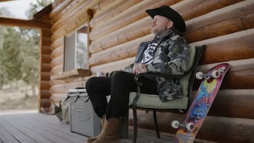 Jason Ellis vestido de cazador con su tabla de skate al lado