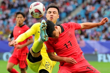 El defensa de Malasia Dion Cools lucha por el balón con el centrocampista de Corea del Sur Hwang Hee-chan durante el encuentro que enfrentó a sus selecciones en la Copa de Asia que se disputa en Qatar. Es tal el ímpetu con el que se emplea el malasio que pudiera parecer que ha confundido la cabeza de su rival con el balón.