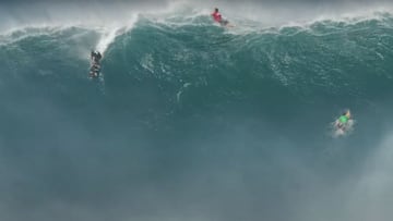 Ola gigante rompiendo en Jaws (Maui, Hawái), con dos surfistas remando para escapar y uno realizando el drop para surfearla.