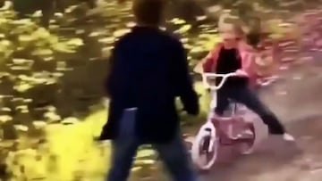 Una niña practicando MTB con una bici pequeña por la montaña, a toda velocidad, con la madre metiéndose delante suyo para frenarla.