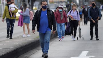 People walk along a road as merchants block it during a protest against the Colombian government's mandatory quarantine imposed for next weekend in some main cities of the country to prevent Covid-19 contagions, in Bogota, on April 15, 2021. (Photo by Raul ARBOLEDA / AFP)
