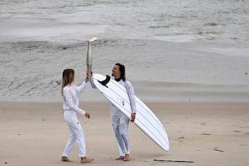 Los surfistas franceses Zoe Grospiron (izquierda) y Edouard Delpero (derecha) sostienen la llama olímpica durante el relevo de la antorcha en la playa entre Biarritz y Anglet.