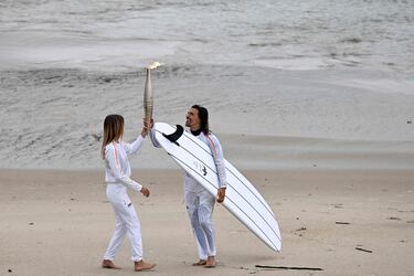 Los surfistas franceses Zoe Grospiron (izquierda) y Edouard Delpero (derecha) sostienen la llama olímpica durante el relevo de la antorcha en la playa entre Biarritz y Anglet.