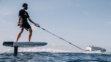 El dron el&eacute;ctrico remolcador de tracci&oacute;n n&aacute;utica funcionando y arrastrando a un foil surfer en el mar, con el cielo despejado. 