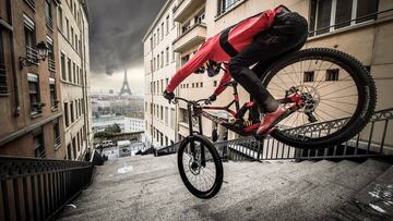 Fabio Wibmer, piloto de MTB, bajando por unas escaleras de Par&iacute;s con su bici, con la Torre Eiffel al fondo.