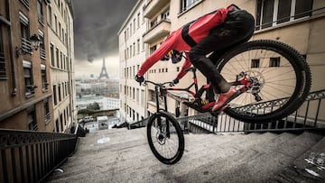 Fabio Wibmer, piloto de MTB, bajando por unas escaleras de París con su bici, con la Torre Eiffel al fondo.