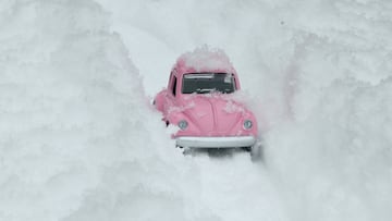 Coche rosa sepultado por la nieve en una ciudad.