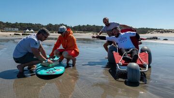 Tres monitores preparan una tabla de surf para una persona con una discapacidad física en una playa de Cantabria.
