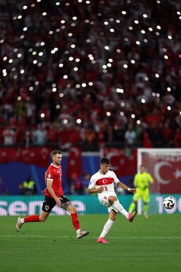 El delantero de Turquía Arda Güler y el defensor de Austria Stefan Posch luchan por el balón durante el partido de octavos mientras que los aficionados iluminan con sus móviles.