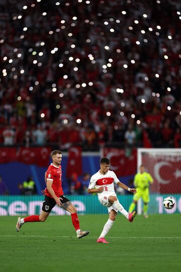 El delantero de Turquía Arda Güler y el defensor de Austria Stefan Posch luchan por el balón durante el partido de octavos mientras que los aficionados iluminan con sus móviles. 