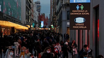 A sign advises people to use masks and social distancing in a crowded commercial street, amid the coronavirus disease (COVID-19) pandemic, in Madrid, Spain, December 20, 2021. REUTERS/Susana Vera