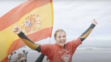 Carmen López saliendo a hombros del agua en La Jolla (California, Estados Unidos) el 14 de marzo del 2020, levantando los brazos en señal de victoria y sonriendo, con una bandera española detrás y unas cuantas olas al fondo de