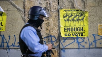 PHILADELPHIA, PA - OCTOBER 28: A police officer walks past a sign that reads &quot;ENOUGH GO VOTE&quot; sign and graffiti that reads &quot;WALTER WALLACE RIP&quot; an hour before a citywide curfew, on October 28, 2020 in Philadelphia, Pennsylvania. Mayor 