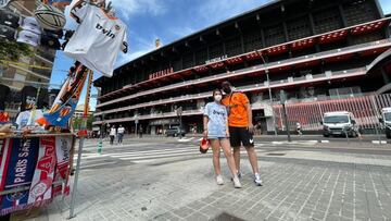 Dos aficionados, junto a un tenderete de venta de bufandas y camisetas en los aleda&ntilde;os de Mestalla. 