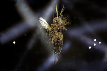 Un viajero interestelar dorado desciende al estadio, convertido en un teatro gigante y misterioso, desde el cielo. Se atenúan las luces para dar paso a una música de suspense.