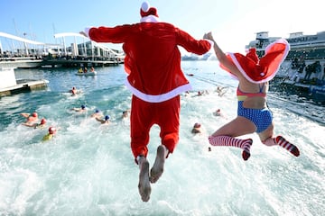 Participantes vestidos con trajes de Santa Claus saltan al agua en el puerto de Barcelona.