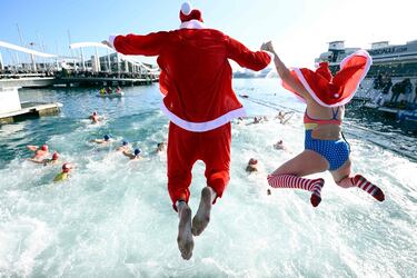 Participantes vestidos con trajes de Santa Claus saltan al agua en el puerto de Barcelona.