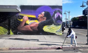 A woman sweeps the street corner in front of a mural of the late Los Angeles Lakers basketball star Kobe Bryant by artist Tehrell Porter in Los Angeles, California on January 25, 2021
