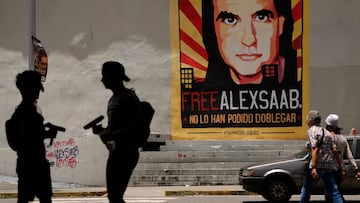 FILE - In this Sept. 9, 2021 file photo, pedestrians walk near a poster of Alex Saab that reads in Spanish "Alex Saab Free. They haven't been able to bend him," in Caracas, Venezuela. Newly unsealed court records show that the Colombian businessman linked to Venezuelan President Nicolas Maduro was secretly signed up by the D.E.A. as a cooperating source in 2018 and gave agents information about bribes he paid to Venezuelan officials. However, he was deactivated as a source after failing to meet a deadline to surrender himself and was indicted in Miami federal court on charges of siphoning millions from state contracts. (AP Photo/Ariana Cubillos, File)