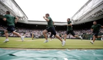 Chicos y chicas recogepelotas corren para cubrir la pista de tenis de Wimbledon para protegerla de la lluvia.