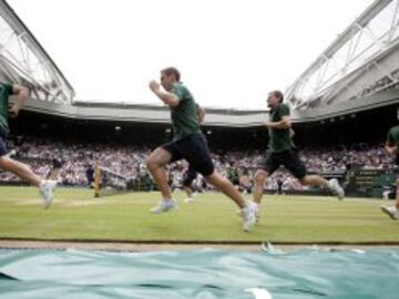 Chicos y chicas recogepelotas corren para cubrir la pista de tenis de Wimbledon para protegerla de la lluvia.