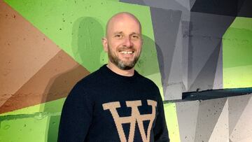 El fundador del festival de action sports y cultura urbana de Vigo, el más importante del sur de Europa, sonriendo ante una pared con un graffiti de colores verdes, grises y marrones.
