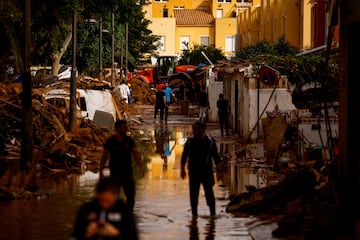 La gente camina por una calle embarrada, tras las inundaciones provocadas por las fuertes lluvias, en Massanassa