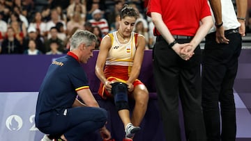 Spain's Carolina Marin is assisted by her coach Fernando Rivas as she puts on a knee band while attempting to continue her women's singles badminton semi-final match against China's He Bing Jiao after an injury, before eventually conceding, during the Paris 2024 Olympic Games at Porte de la Chapelle Arena in Paris on August 4, 2024. (Photo by Luis TATO / AFP)