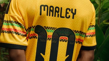 Una base llamativa de franjas horizontales en verde, dorado y rojo crea un divertido patrón repetitivo que evoca las icónicas prendas y gorros de crochet asociados a Bob Marley.