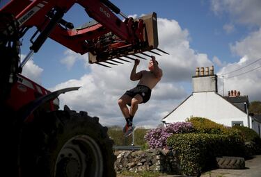 El escocés Alex Craig, jugador internacional de rugby, realiza dominadas en la pala de un tractor en la granja de sus padres en Castle Douglas, Escocia. Craig, que actualmente juega en el Gloucester de la Premiership inglesa, se ha visto obligado a adaptarse a las circunstancias para no perder la forma durante el confinamiento.