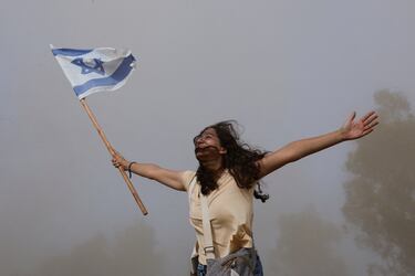 Una persona que sostiene una bandera israelí reacciona en medio del polvo mientras un helicóptero que transporta rehenes liberados, que han estado retenidos en Gaza desde el mortal ataque del 7 de octubre de 2023 por Hamas.