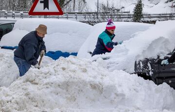 Unos vecinos quitan la nieve de sus vehiculos en el pueblo de Pajares. La autopista del Huerna (AP-66), principal vía de comunicación entre Asturias y León, está ya reabierta al tránsito de camiones tras las intensas nevadas de las últimas horas. 