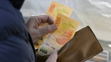 A customer takes two thousand Argentine pesos (about 14 US dollars) from her wallet to pay for groceries at a fruit and vegetable store in Buenos Aires on August 9, 2022. (Photo by JUAN MABROMATA / AFP) (Photo by JUAN MABROMATA/AFP via Getty Images)