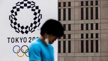 Un hombre con la mascarilla bajada pasa en frente del logo de Tokio 2020