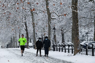 Una persona corre en la calle junto a una pareja que pasea por uno de los parques de Londres. 