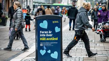 People walk past a trash can with a sign reading &quot;The danger is not over - Keep your distance&quot; in a pedestrian street in central Uppsala, Sweden, on Octtober 21, 2020. - Due to an increase of coronavirus Covid-19 cases in the region of Uppsala, 