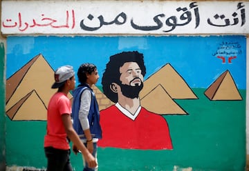 Egyptian youths walk in front of a picture of Liverpool's Egyptian forward Mohamed Salah with background of Great Pyramids, in Cairo, Egypt May 2, 2018. Arabic words read "You are stronger than drugs".