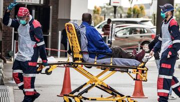 An emergency paramedic wearing full COVID-19 coronavirus personal protective equipment (PPE) flashes the victory sign as they arrive with a patient at the Greenacres Hospital in Port Elizabeth, on July 10, 2020. - Ambulances have to queue before patients